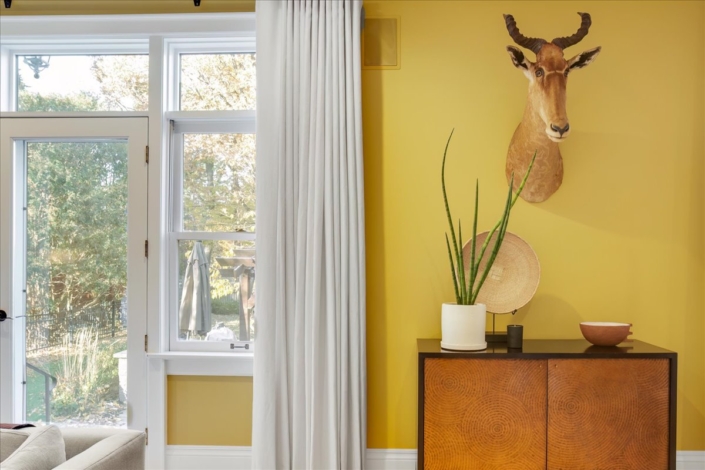 Sideboard with animal head, plant and basket by window with pinch pleat custom drapery