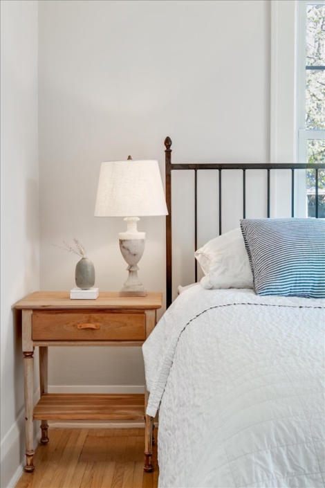 Bedroom vignette with natural wood night stand, marble lamp and white bedding with a blue pillow