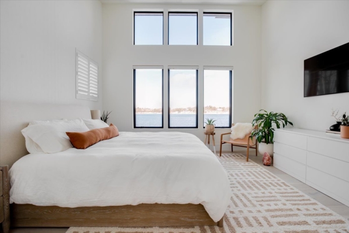 Master bedroom with lake view and pops of ochre color, side chair and plant