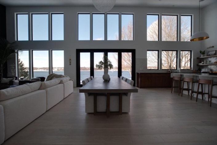 Wood dining table in center of room with natural fabric chairs and a view of the lake