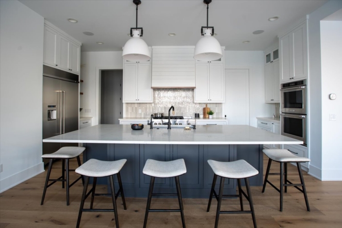 blue kitchen island with stools and tile backsplash, white cabinets