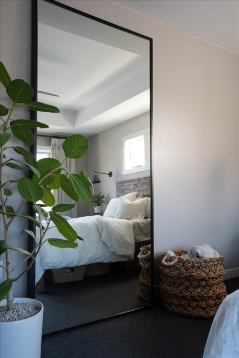 Master bedroom with bed reflected in mirror and tall plant