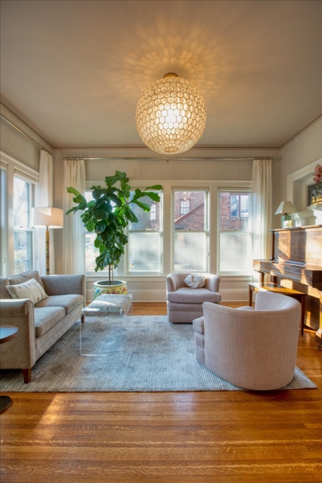 Sunroom with large plant, capiz light, curved pale pink swivel chairs and piano