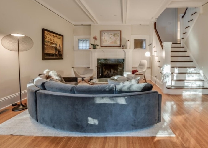 Living room with curved blue sofa, side chairs, fireplace and stairway