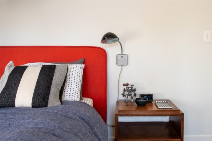 Boys bedroom with red headboard, gray tone bedding, nightstand and radar sconce