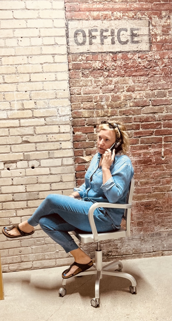 Jen on phone with Office brick wall behind her